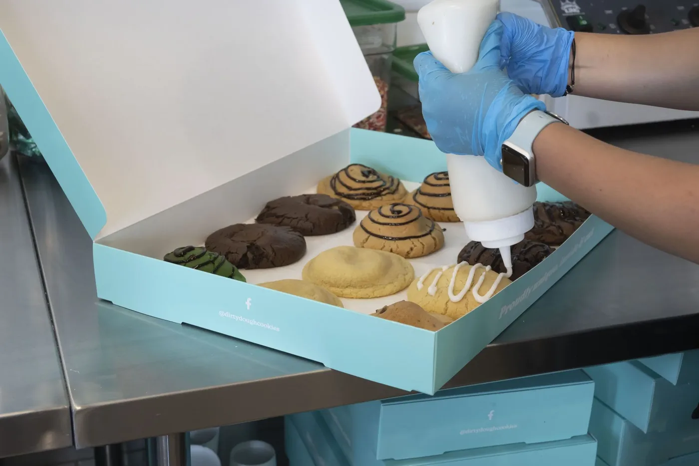 A Dirty Dough catering box being filled with an assortment of stuffed cookies, cinnamon rolls, and bars